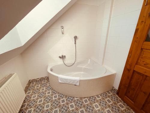 A cozy attic bathroom with a corner bathtub, patterned floor tiles, wooden accents, and a warm, inviting atmosphere ideal for travelers seeking a quaint and comfortable stay.
