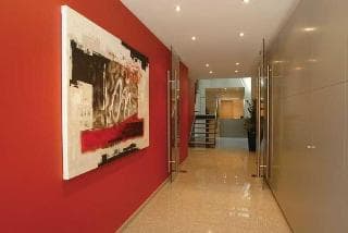 A modern hotel corridor features a vibrant red wall adorned with an abstract painting, creating a stylish and inviting atmosphere ideal for travelers seeking contemporary accommodations.