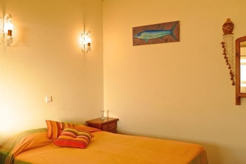 A cozy hotel room features a warmly lit bed adorned with orange bedding, a fish painting on the wall, and decorative sconces, ideal for travelers seeking a comfortable and inviting stay.
