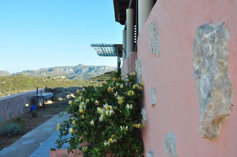 A serene outdoor patio with a pink wall adorned with stone accents overlooks a picturesque mountainous landscape, ideal for travelers seeking a tranquil retreat in a rustic setting.