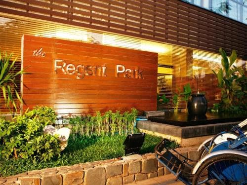 A serene urban oasis featuring "The Regent Park" sign amidst lush greenery and modern architecture, ideal for travelers seeking a tranquil accommodation experience.