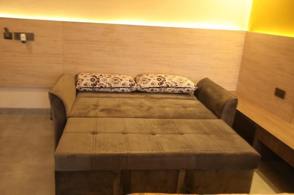 A cozy hotel room features a plush convertible sofa bed adorned with patterned pillows against a warmly lit wooden wall, ideal for travelers seeking comfort and relaxation.