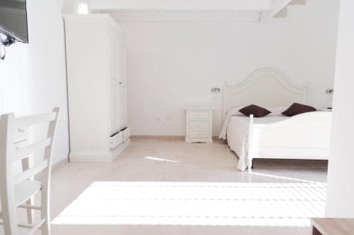 A serene minimalist bedroom with white furniture, soft lighting, and a cozy bed invites travelers seeking a peaceful retreat for restful stays.