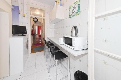 A cozy apartment kitchenette features white tiled walls, a microwave on the counter, and a hallway leading to a bedroom, ideal for travelers seeking compact and functional living spaces.