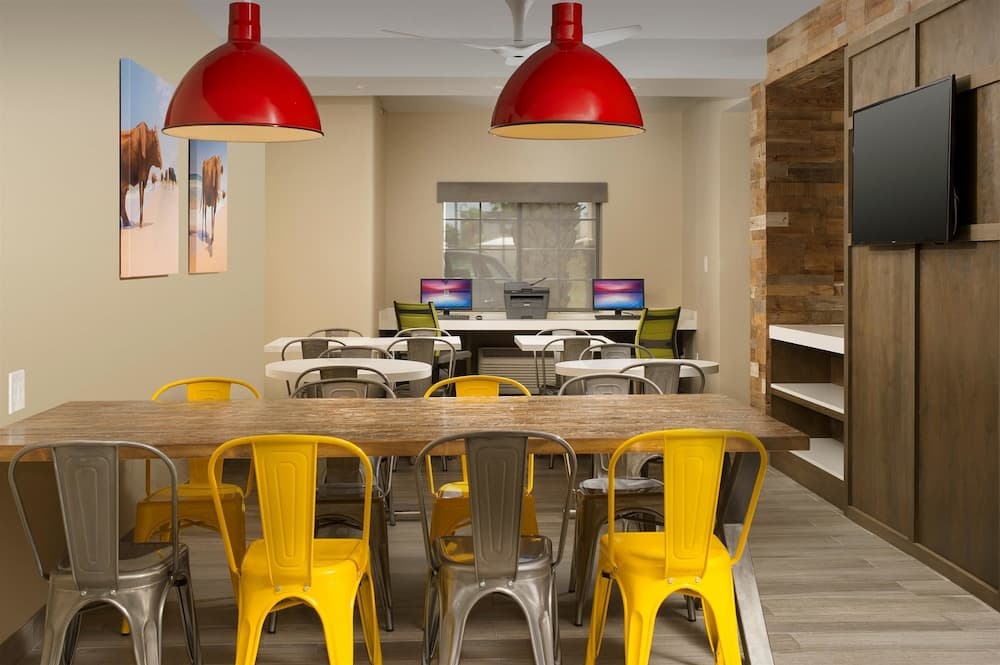A vibrant co-working space features colorful yellow chairs, wooden tables, red pendant lights, and modern decor, ideal for travelers seeking a productive and stylish work environment.