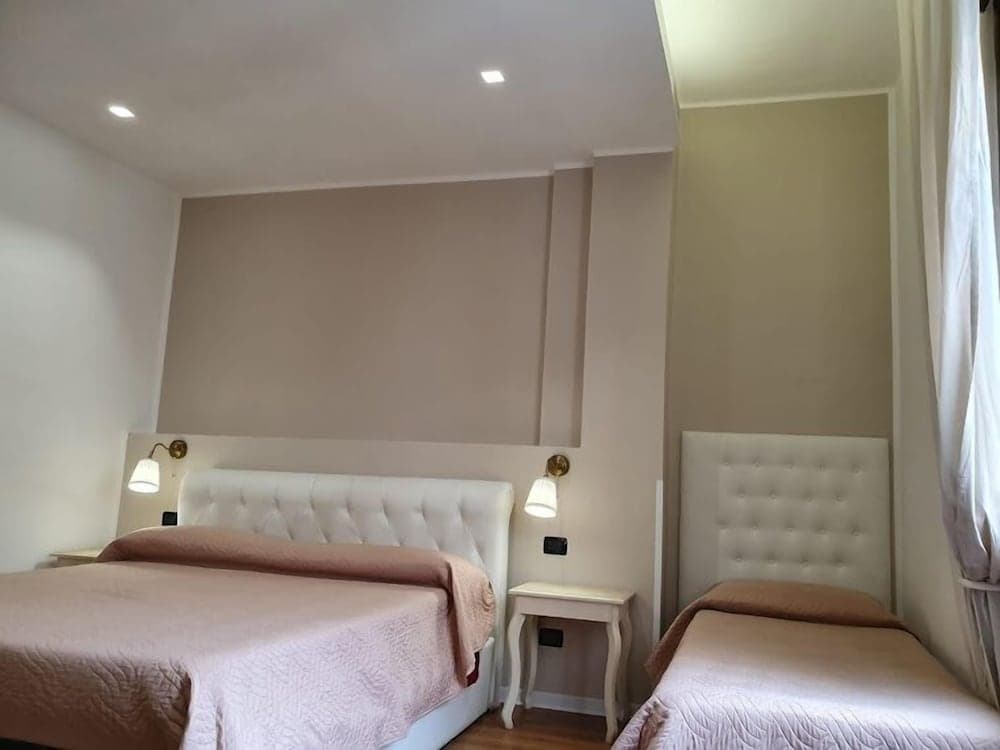 A cozy hotel room features two neatly made beds with tufted headboards, soft pink bedding, and wall-mounted lamps, creating a warm and inviting atmosphere ideal for travelers seeking comfort and relaxation.