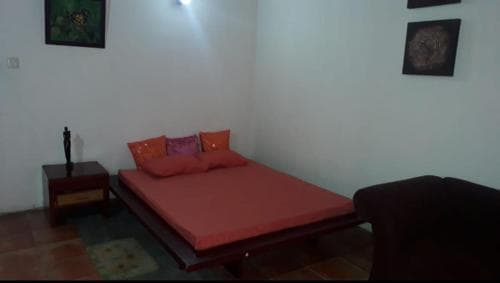 A cozy bedroom with a vibrant red bedspread, wooden furniture, and framed artwork creates a serene atmosphere, ideal for travelers seeking a comfortable and artistic retreat.