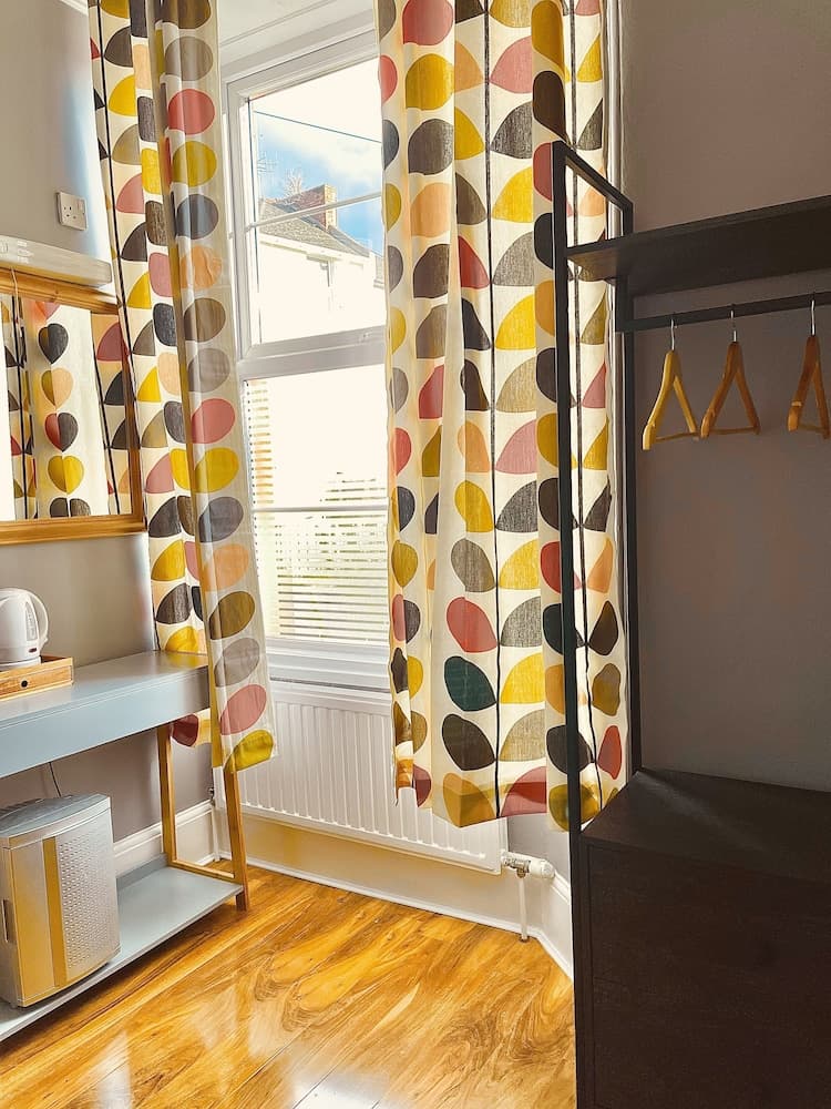 A cozy bedroom with vibrant patterned curtains, wooden flooring, and a modern wardrobe exudes warmth and comfort, ideal for travelers seeking a stylish and inviting accommodation.