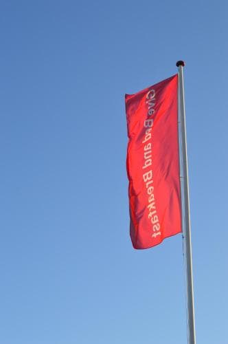 A vibrant red flag with white text flutters against a clear blue sky, creating an uplifting scene ideal for outdoor events or promotional activities.
