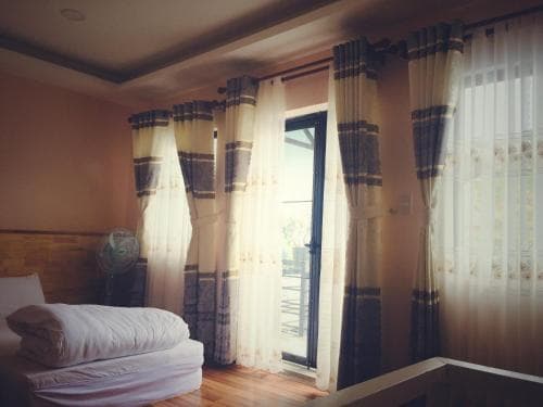 A cozy bedroom with wooden floors, patterned curtains, and soft natural light creates a serene atmosphere, ideal for travelers seeking relaxation in a homely accommodation.