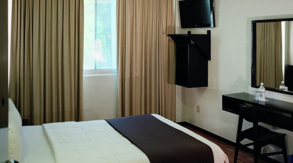 A cozy hotel room features a neatly made bed, a desk with a mirror, and a wall-mounted TV, creating a comfortable atmosphere ideal for travelers seeking relaxation.