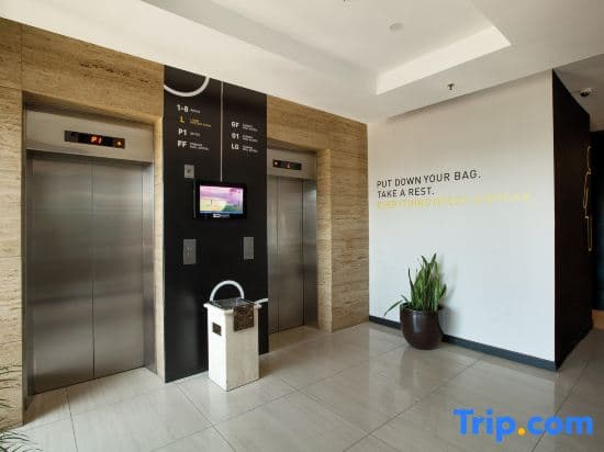 A modern hotel lobby features sleek stainless steel elevators, motivational wall text, and a potted plant, creating a welcoming atmosphere ideal for travelers seeking a quick rest during their journey.