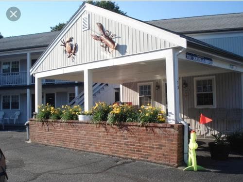 A charming motel entrance adorned with deer sculptures and vibrant flower beds invites travelers to a cozy stay in a serene suburban setting.