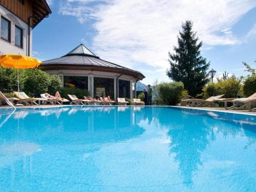 A serene outdoor pool surrounded by lounge chairs and a pavilion under a clear sky, ideal for relaxing at a mountain resort getaway.