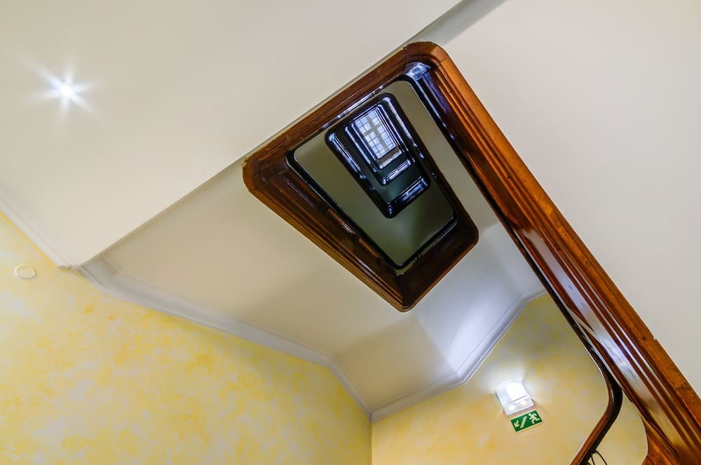 A warmly lit spiral staircase with yellow walls and wooden railings creates an inviting atmosphere, perfect for travelers exploring cozy indoor spaces in boutique hotels or historic buildings.