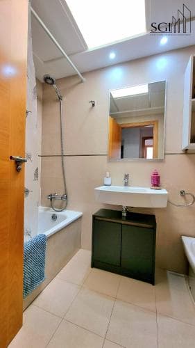 A cozy, well-lit bathroom with a bathtub, sink, mirror, and tiled floor offers a serene space for travelers seeking comfort and cleanliness during their stay.