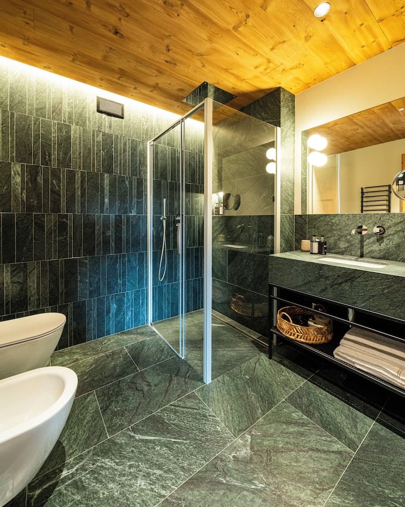 A luxurious bathroom with green marble tiles, a wooden ceiling, and modern fixtures creates a serene and elegant atmosphere, ideal for high-end accommodation or spa retreats.