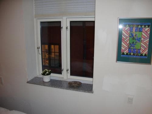A cozy indoor space features a double-paned window with a small potted plant on the sill, a decorative bowl, and a colorful framed artwork on the wall, ideal for travelers seeking a quiet and artistic accommodation setting.