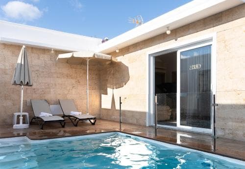 A serene rooftop patio features a small pool, lounge chairs under umbrellas, and a glass door leading indoors, ideal for a relaxing vacation retreat.