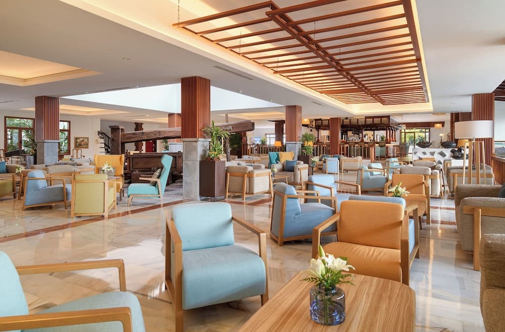 A spacious hotel lobby with modern wooden furniture, vibrant blue and orange chairs, and a warm, inviting atmosphere is ideal for travelers seeking relaxation and comfort during their stay.