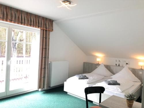 A cozy hotel room with a neatly made bed, green carpet, and a balcony offering a serene forest view, ideal for travelers seeking relaxation and comfort.