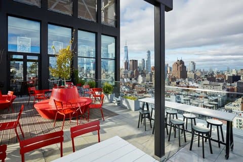 A vibrant rooftop terrace at citizenM New York Bowery offers panoramic city views with modern red seating, ideal for travelers seeking a stylish urban retreat.
