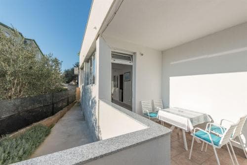 A cozy balcony with a tiled floor, white chairs, and a table set against a sunny backdrop, perfect for a relaxing vacation retreat.