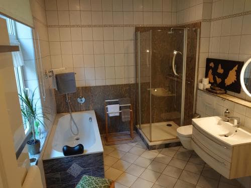 A cozy, well-lit bathroom featuring a bathtub, glass-enclosed shower, wooden vanity, and potted plant, ideal for travelers seeking comfort and cleanliness in their accommodations.