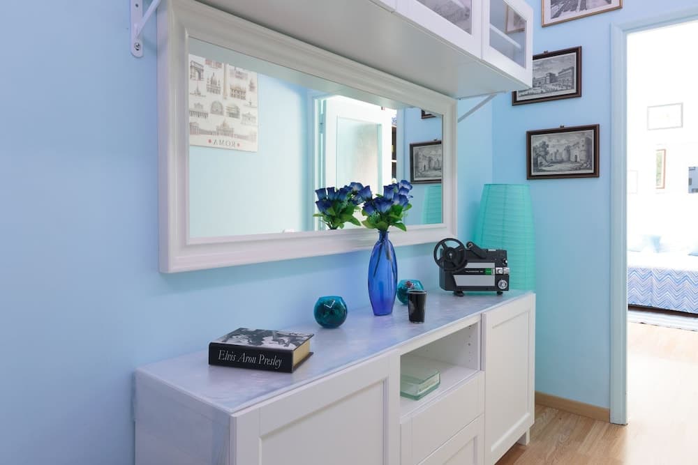 A serene blue-themed entryway features a white console table adorned with a vase of blue flowers, a vintage projector, and framed artwork, ideal for travelers seeking cozy and stylish accommodations.