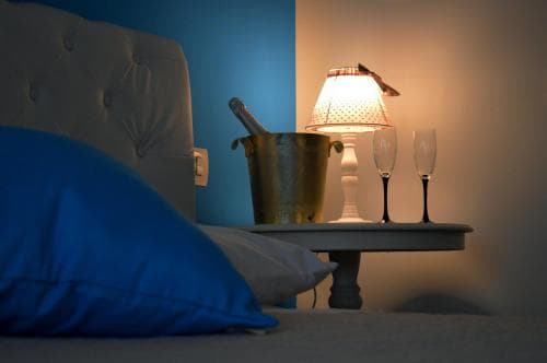 A cozy hotel room bedside scene features a softly lit lamp, champagne flutes, and an ice bucket, creating an intimate and romantic atmosphere ideal for a couples' getaway.