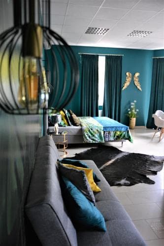 A cozy modern living room with teal walls, stylish furniture including a gray sofa and bed adorned with vibrant textiles, and decorative elements like a cowhide rug and unique pendant light, ideal for travelers seeking a chic and comfortable stay.