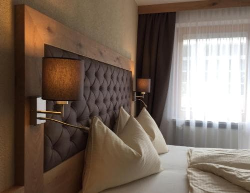 A cozy hotel room features a neatly made bed with plush pillows against a stylish tufted headboard, framed by warm wooden accents and soft lighting, ideal for travelers seeking comfort and relaxation.