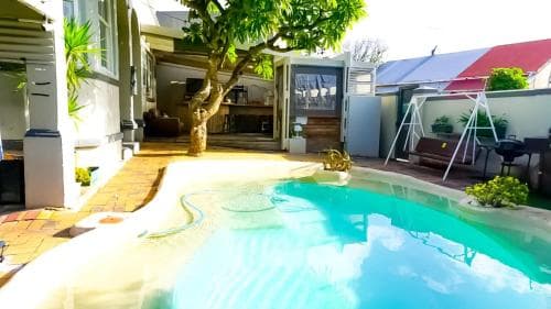 A serene backyard oasis features a sparkling pool surrounded by lush greenery, cozy seating areas, and a charming tree, ideal for relaxing getaways or family vacations.