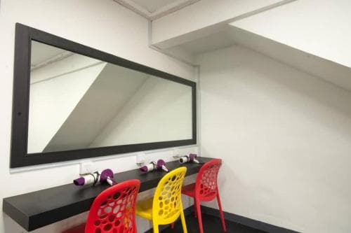 A cozy attic space features a sleek black vanity with colorful chairs under a large mirror, ideal for travelers seeking a stylish makeup or grooming area in boutique accommodations.