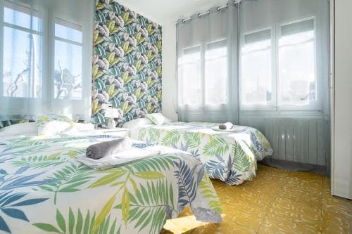 A cozy hotel room with vibrant tropical-patterned bedding, yellow tiled floors, and large windows draped in sheer curtains, evokes a cheerful and inviting atmosphere ideal for travelers seeking comfort and style.