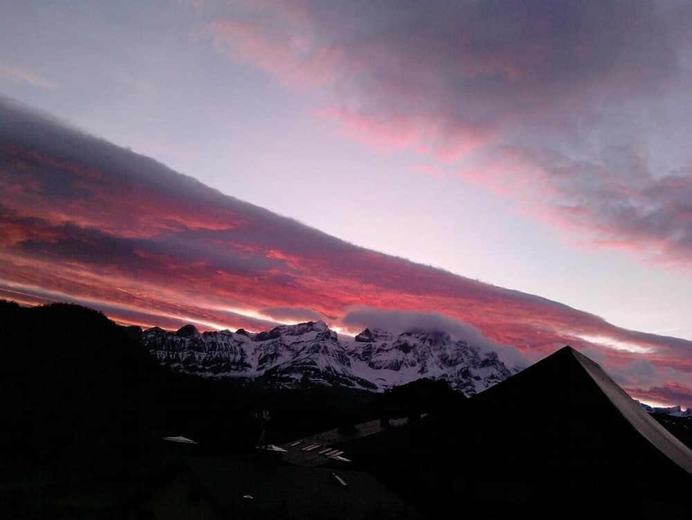 A serene mountain village at dusk showcases snow-capped peaks under a vibrant pink and purple sky, ideal for travelers seeking tranquil alpine retreats.