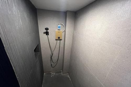 A modern, minimalist shower room with sleek gray tiles and a mounted digital control panel offers a clean and functional space ideal for travelers seeking efficient accommodations.