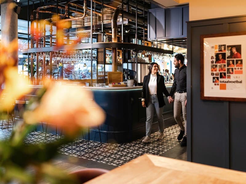 A cozy, stylish hotel bar at the ibis Amsterdam Centre features a couple enjoying a warm conversation amidst modern decor, patterned flooring, and a vibrant atmosphere ideal for travelers seeking a welcoming urban retreat.