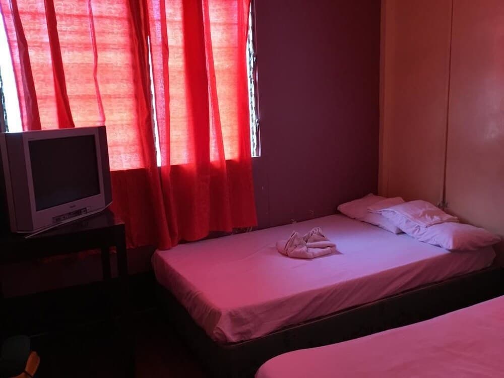 A cozy budget hotel room features soft pink bedding, red curtains filtering natural light, and a vintage TV, ideal for travelers seeking affordable accommodations with a warm ambiance.