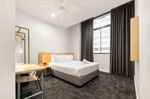 A cozy urban hotel room features a neatly made bed, modern furnishings, and large windows with city views, ideal for travelers seeking comfort and convenience in a bustling metropolis.