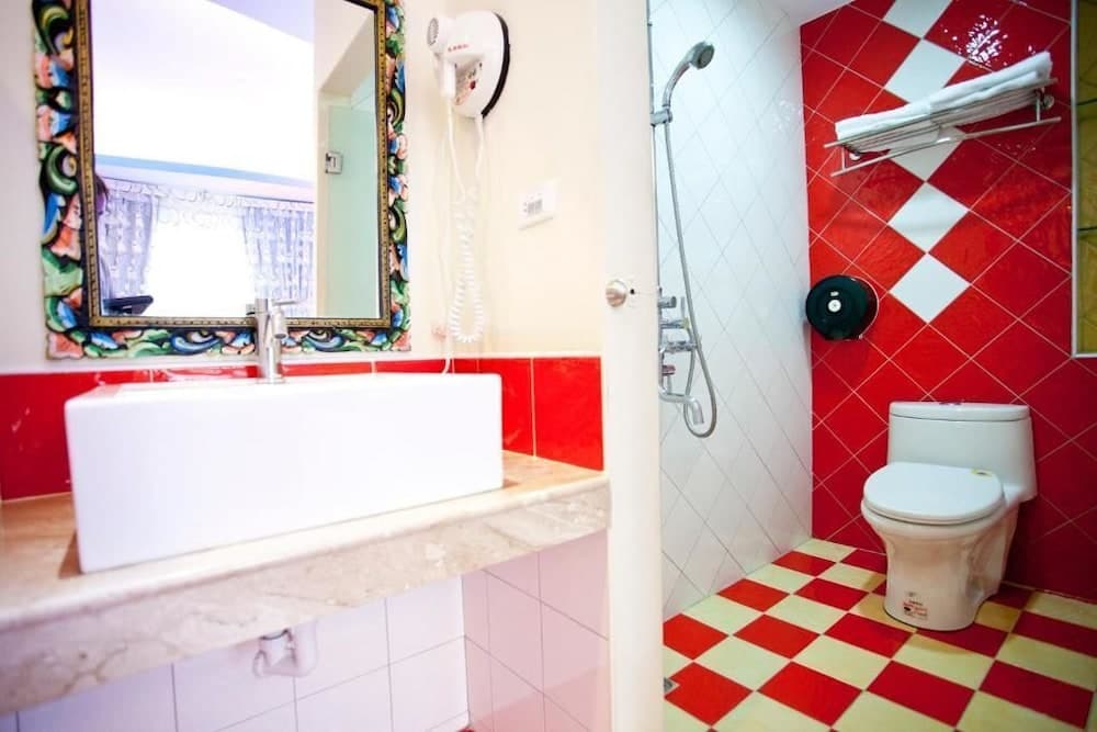 A vibrant bathroom with red and white checkered tiles, a colorful mirror frame, and modern fixtures offers a cheerful and functional space for travelers seeking comfort and style.