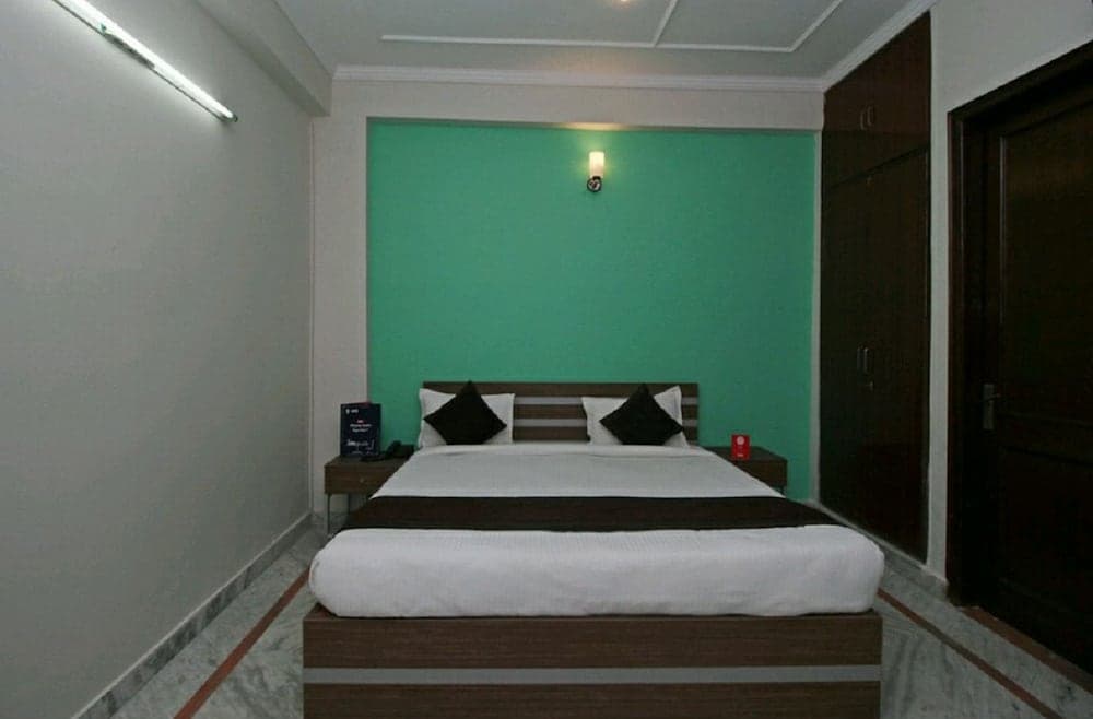 A cozy hotel room features a neatly made bed with white linens against a vibrant green accent wall, ideal for travelers seeking comfort and simplicity.