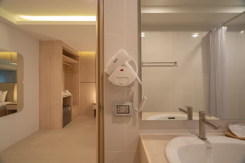 A cozy hotel bathroom with a mounted hairdryer, sleek sink, and adjacent walk-in closet creates a warm and inviting atmosphere ideal for travelers seeking comfort and convenience.