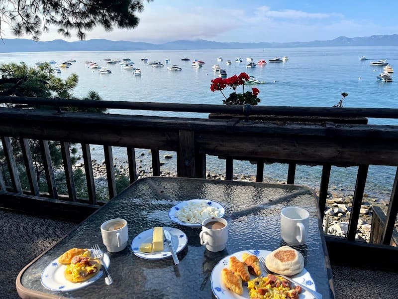 Enjoy a serene lakeside breakfast on a wooden balcony overlooking calm waters dotted with boats, perfect for a tranquil holiday retreat in a picturesque lakeside setting.