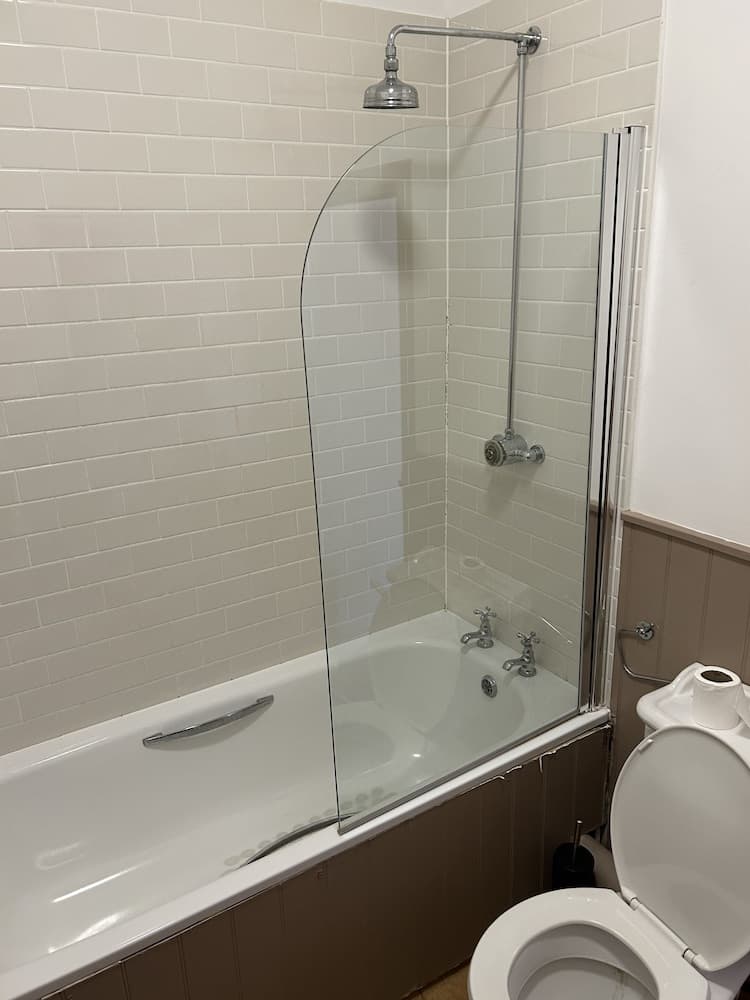 A clean, modern bathroom with white subway tiles, a bathtub with a glass shower screen, and a toilet, ideal for travelers seeking comfortable accommodations.