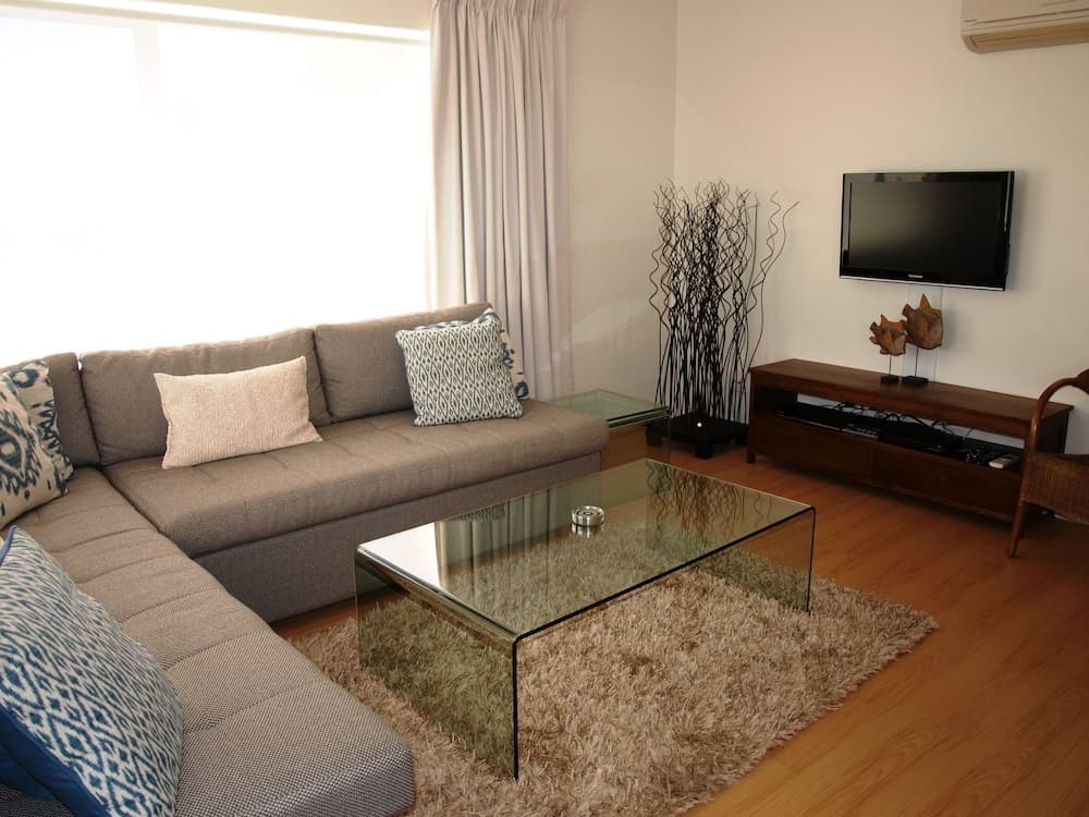 A cozy living room with a sectional sofa, glass coffee table, wooden TV stand, and soft lighting creates a serene atmosphere ideal for travelers seeking comfort in a vacation rental.