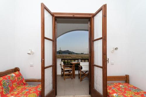 A cozy bedroom with vibrant red bedding opens to a serene balcony view of distant hills, ideal for travelers seeking relaxation in a quaint retreat.