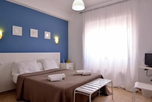 A cozy hotel room with a neatly made bed, blue accent wall, soft lighting, and a small desk by the window, ideal for travelers seeking comfort and relaxation.