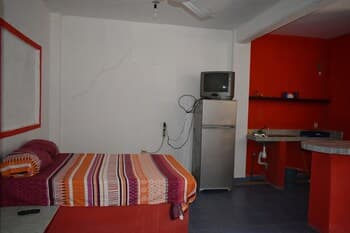 A cozy budget-friendly studio apartment features a vibrant striped bedspread, a small kitchenette with red accents, and a retro television, ideal for solo travelers seeking simplicity and comfort.