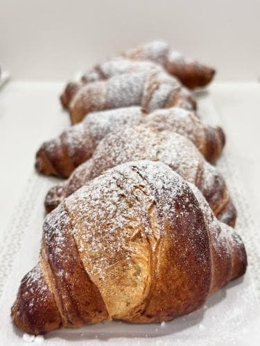 A row of golden, powdered croissants on a white surface evokes a cozy bakery atmosphere, perfect for travelers seeking a delightful continental breakfast experience.
